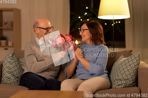 Image of happy senior couple with bunch of flowers at home