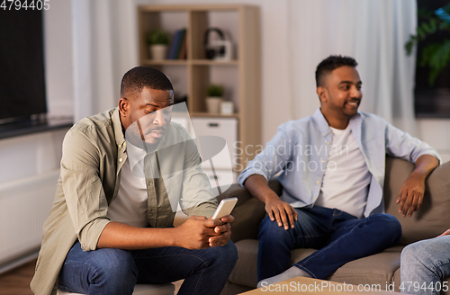 Image of man using smartphone while friends talking at home