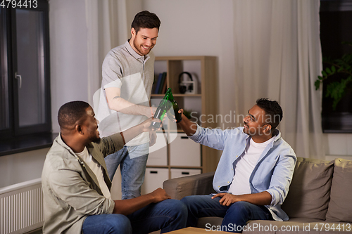 Image of happy male friends drinking beer at home at night