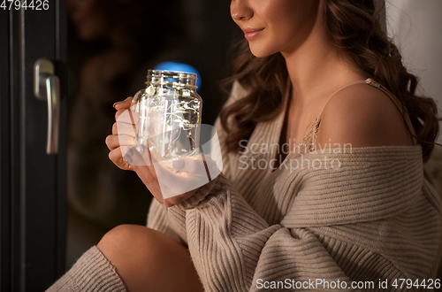 Image of woman with garland lights in glass mug at home