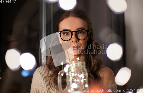 Image of woman with garland lights in glass mug at home