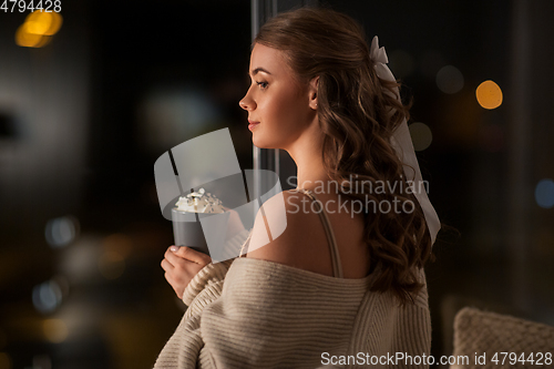 Image of woman holding mug with whipped cream at night