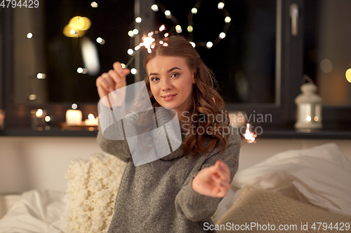 Image of happy young woman with sparklers in bed at home