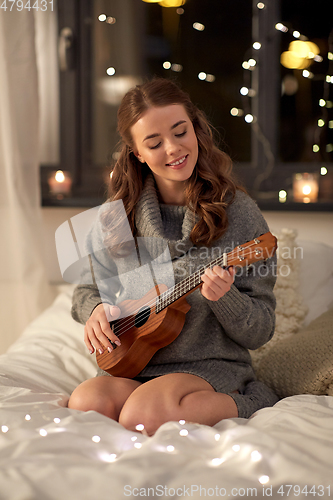 Image of happy young woman playing guitar in bed at home
