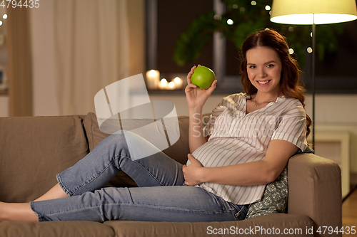 Image of happy pregnant woman with green apple at home