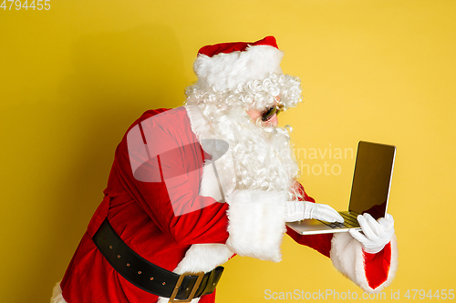 Image of Santa Claus with modern gadgets isolated on yellow studio background