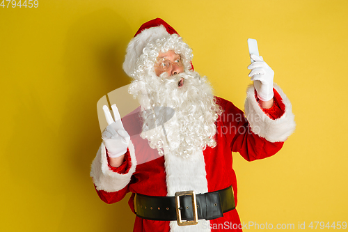 Image of Santa Claus with modern gadgets isolated on yellow studio background