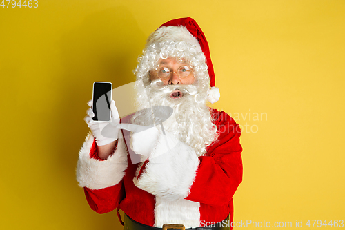 Image of Santa Claus with modern gadgets isolated on yellow studio background