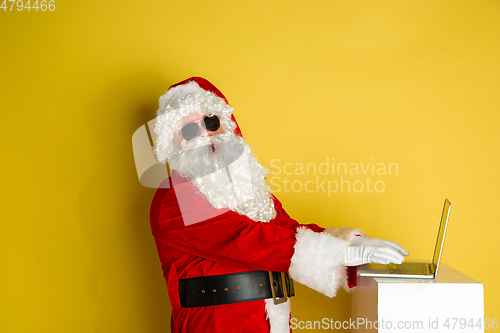 Image of Santa Claus with modern gadgets isolated on yellow studio background