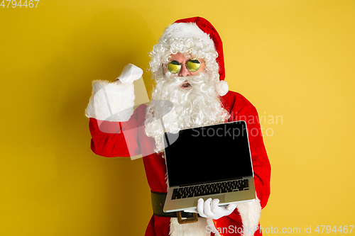 Image of Santa Claus with modern gadgets isolated on yellow studio background