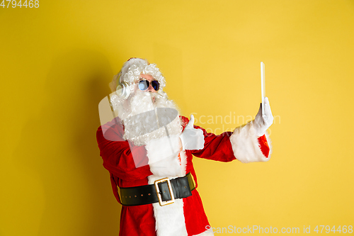 Image of Santa Claus with modern gadgets isolated on yellow studio background