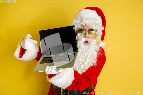 Image of Santa Claus with modern gadgets isolated on yellow studio background