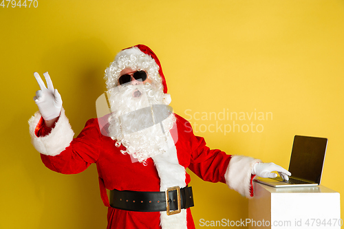 Image of Santa Claus with modern gadgets isolated on yellow studio background