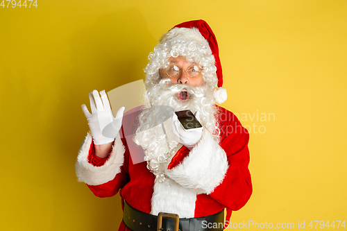 Image of Santa Claus with modern gadgets isolated on yellow studio background