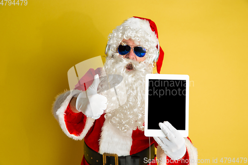 Image of Santa Claus with modern gadgets isolated on yellow studio background