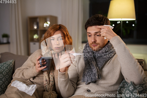 Image of sick couple with thermometer and tea at home