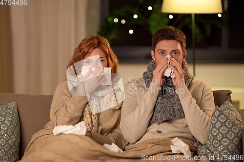 Image of sick young couple with tissue blowing nose at home