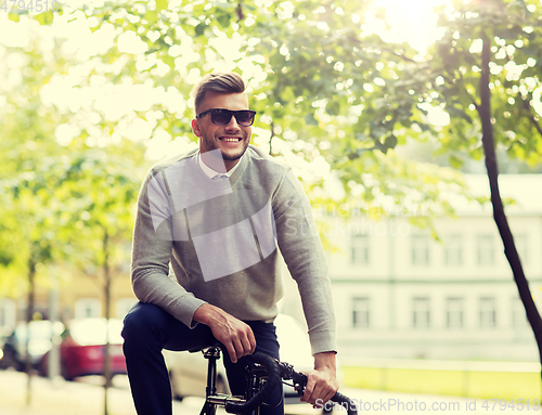 Image of young man in shades riding bicycle on city street