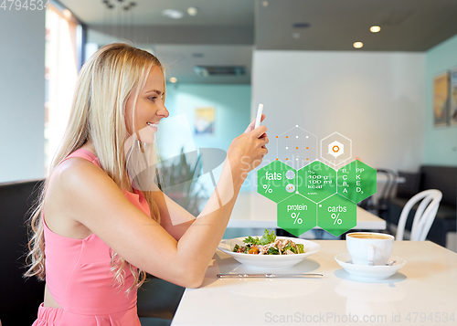 Image of happy woman with smartphone eating at restaurant