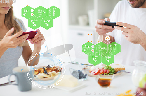 Image of couple with smartphones having breakfast at home