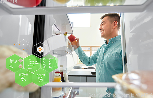 Image of man taking apple from fridge at home kitchen