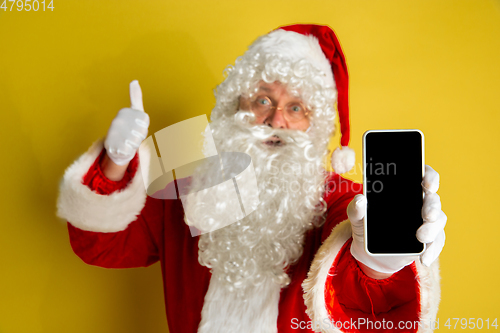 Image of Santa Claus with modern gadgets isolated on yellow studio background