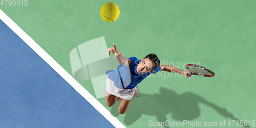 Image of Young woman in blue shirt playing tennis. Youth, flexibility, power and energy.