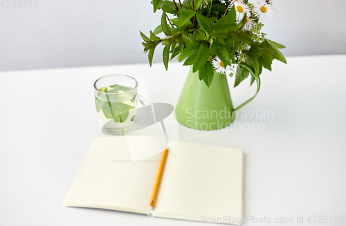 Image of herbal tea, notebook and flowers in jug on table