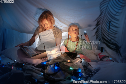 Image of Mother and daughter sitting in a teepee, reading stories with the flashlight