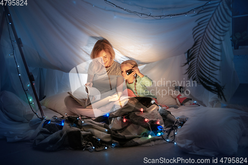 Image of Mother and daughter sitting in a teepee, reading stories with the flashlight