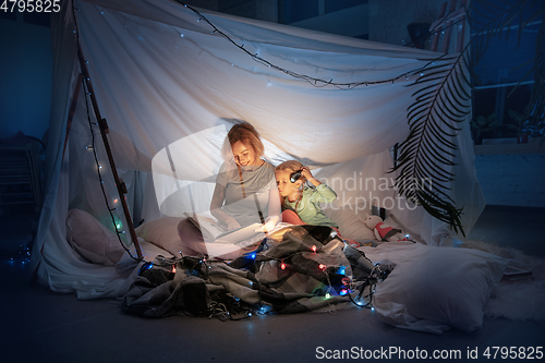 Image of Mother and daughter sitting in a teepee, reading stories with the flashlight