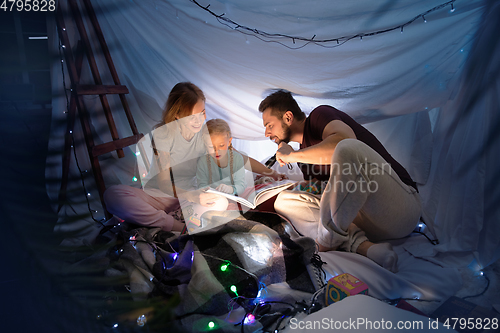 Image of Family sitting in a teepee, reading stories with the flashlight