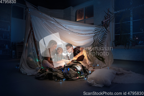 Image of Family sitting in a teepee, reading stories with the flashlight