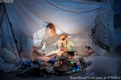 Image of Mother and daughter sitting in a teepee, reading stories with the flashlight