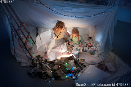 Image of Mother and daughter sitting in a teepee, reading stories with the flashlight