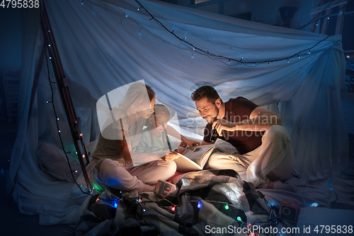 Image of Family sitting in a teepee, reading stories with the flashlight