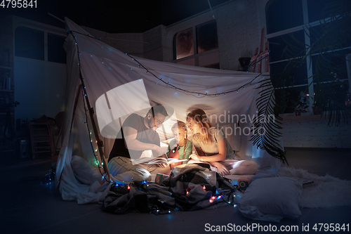 Image of Family sitting in a teepee, reading stories with the flashlight