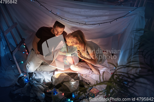 Image of Family sitting in a teepee, reading stories with the flashlight