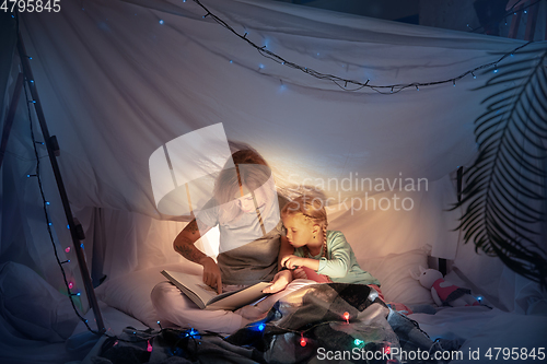 Image of Mother and daughter sitting in a teepee, reading stories with the flashlight