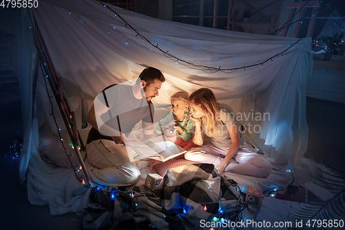 Image of Family sitting in a teepee, reading stories with the flashlight