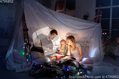 Image of Family sitting in a teepee, reading stories with the flashlight