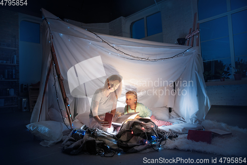 Image of Mother and daughter sitting in a teepee, reading stories with the flashlight