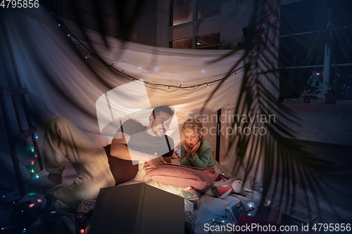 Image of Father and daughter sitting in a teepee, having fun with the flashlight