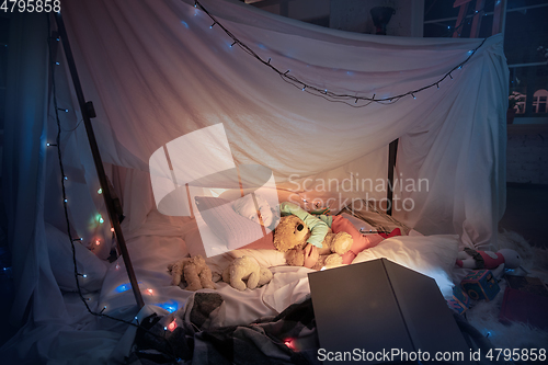 Image of Little girl lying in a teepee, sleeping with the flashlight