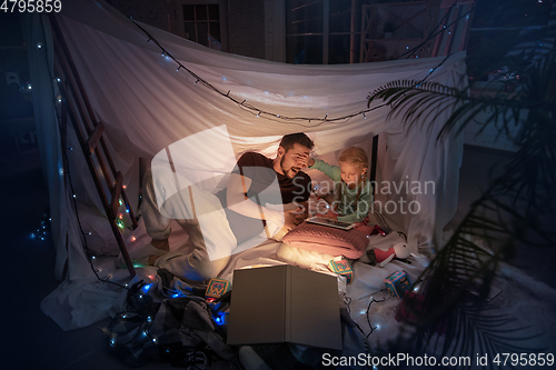 Image of Father and daughter sitting in a teepee, having fun with the flashlight