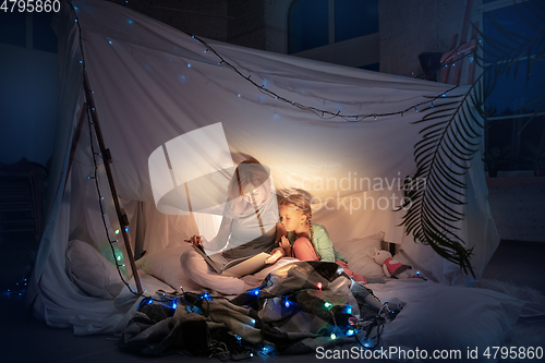 Image of Mother and daughter sitting in a teepee, reading stories with the flashlight