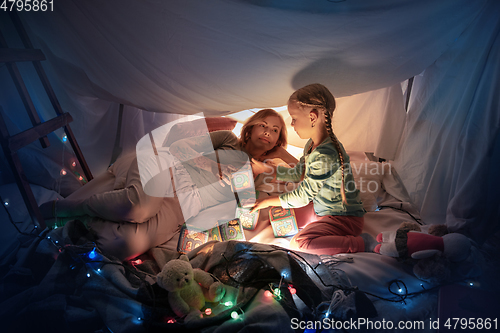 Image of Mother and daughter sitting in a teepee, having fun with the flashlight
