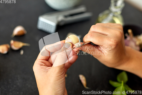 Image of hands peeling garlic with knife for pesto sauce