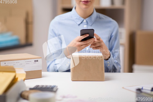 Image of woman with smartphone and parcels at post office