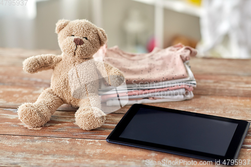 Image of baby clothes, teddy bear toy and tablet computer